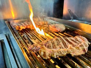 Chuletones de carne roja cocinándose a la parrilla con fuego vivo en la cocina del restaurante Zeppelin Torrelodones