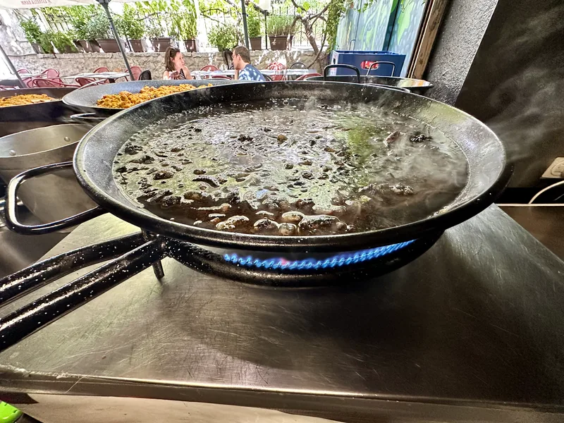 Arroz negro hirviendo en la paellera sobre el fogón con el caldo de tinta aún a la vista